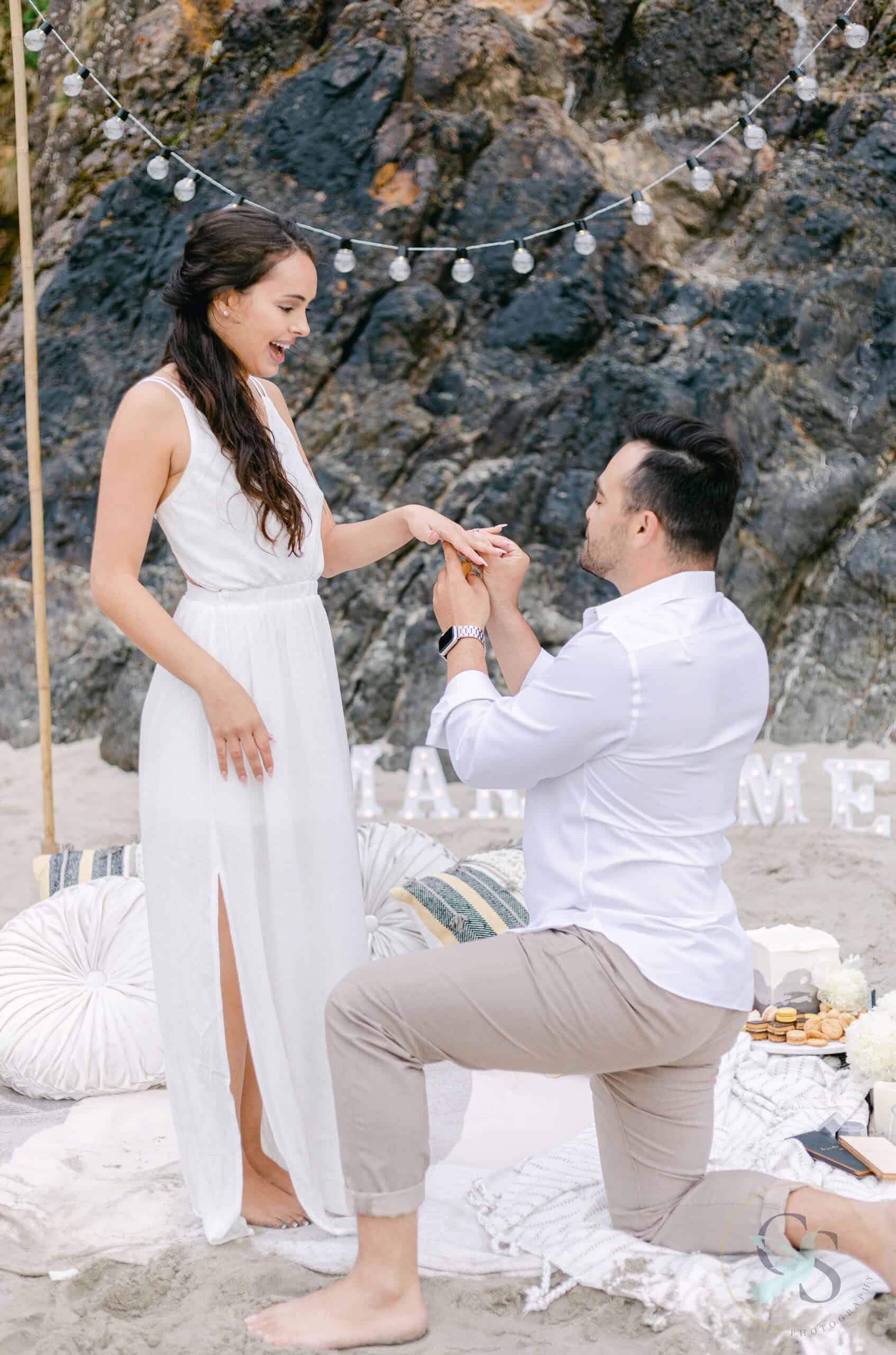Romantic beach proposal with a couple exchanging rings under string lights.